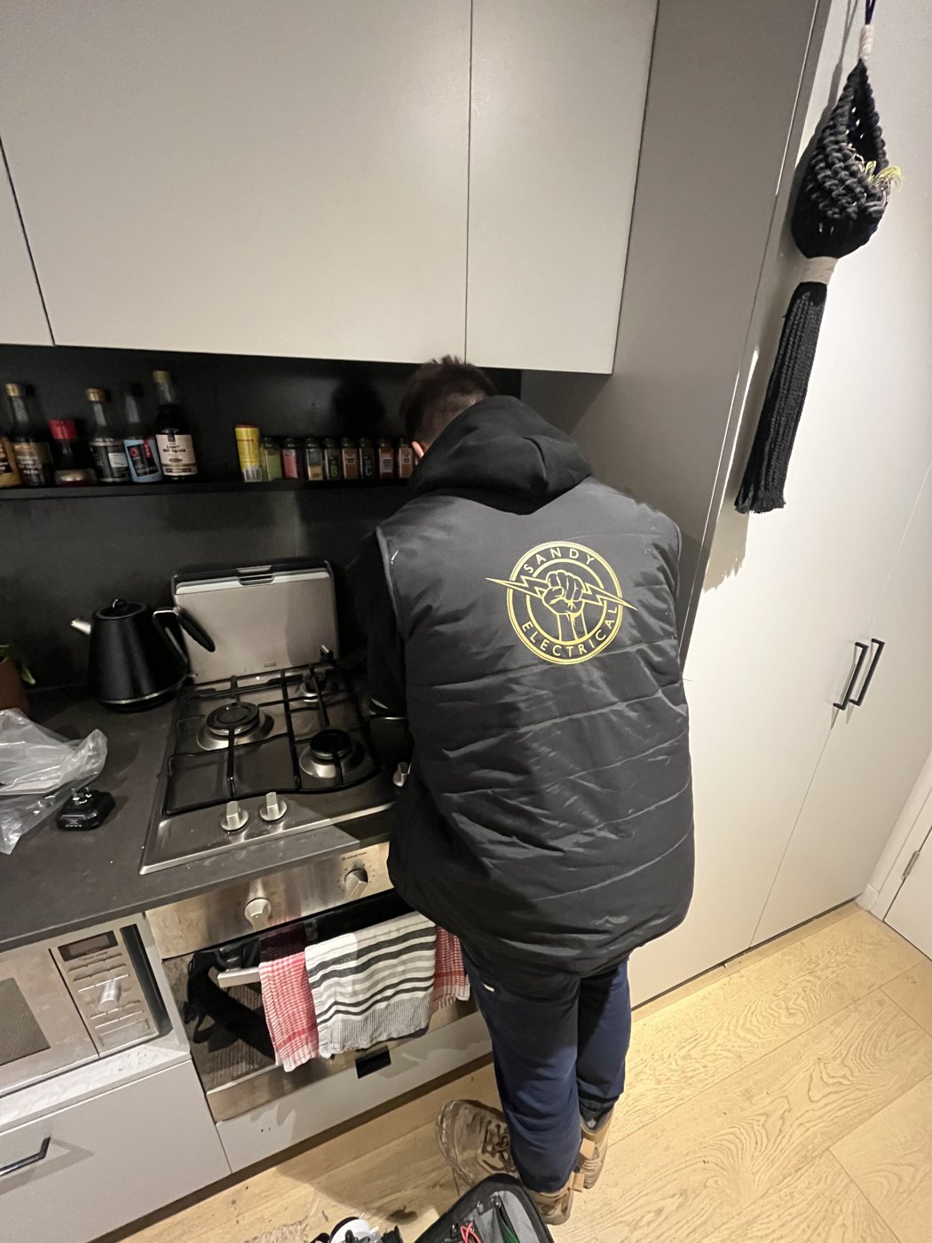 Tyson from Sandy Electrical wearing branded workwear on a kitchen appliance install