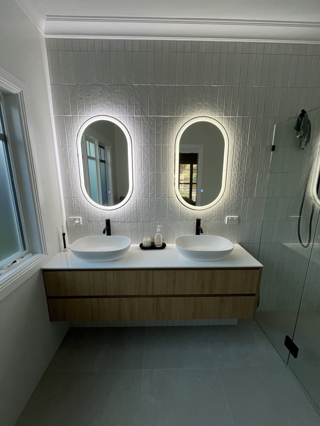 Twin backlit oval LED mirrors above a double bathroom vanity, wide view