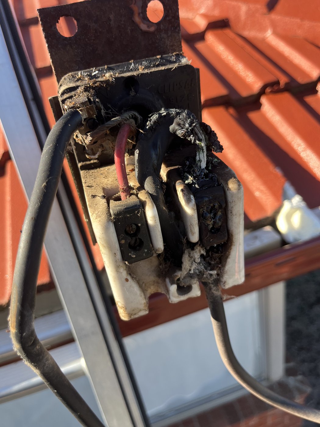 Burnt out mains point-of-attachment fuse assembly on a tiled roof, before repair