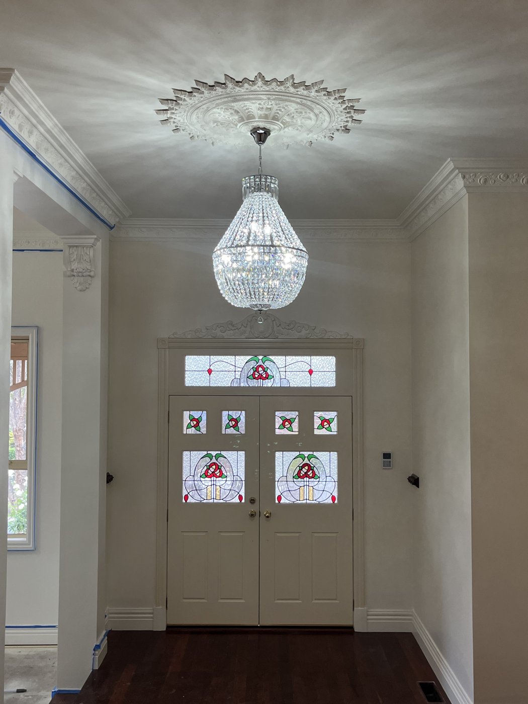 Crystal chandelier installed in an entry hall with ornate ceiling rose