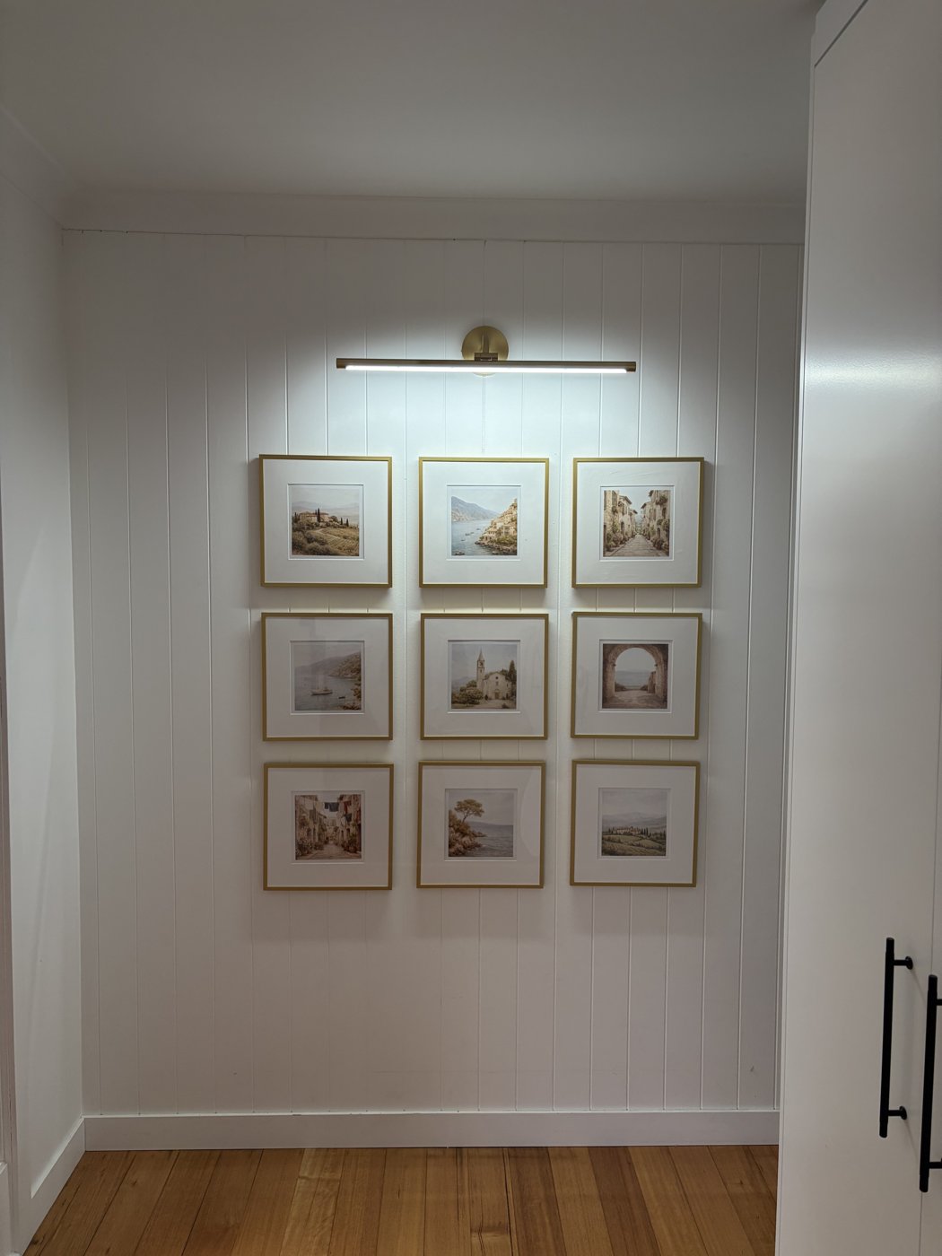 Brass picture light installed above a gallery wall of framed prints in a hallway