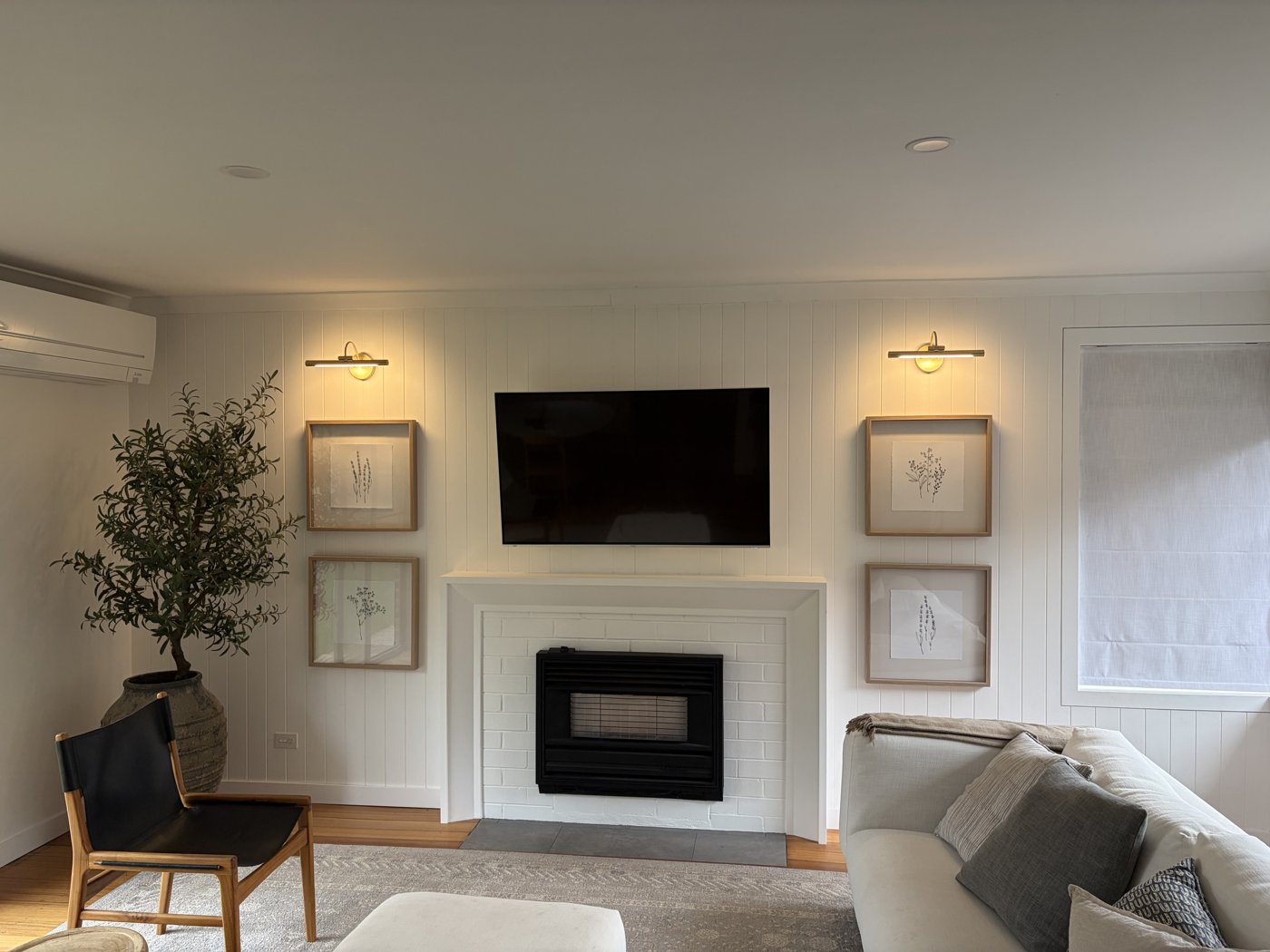 Brass picture lights installed either side of a fireplace above framed artwork