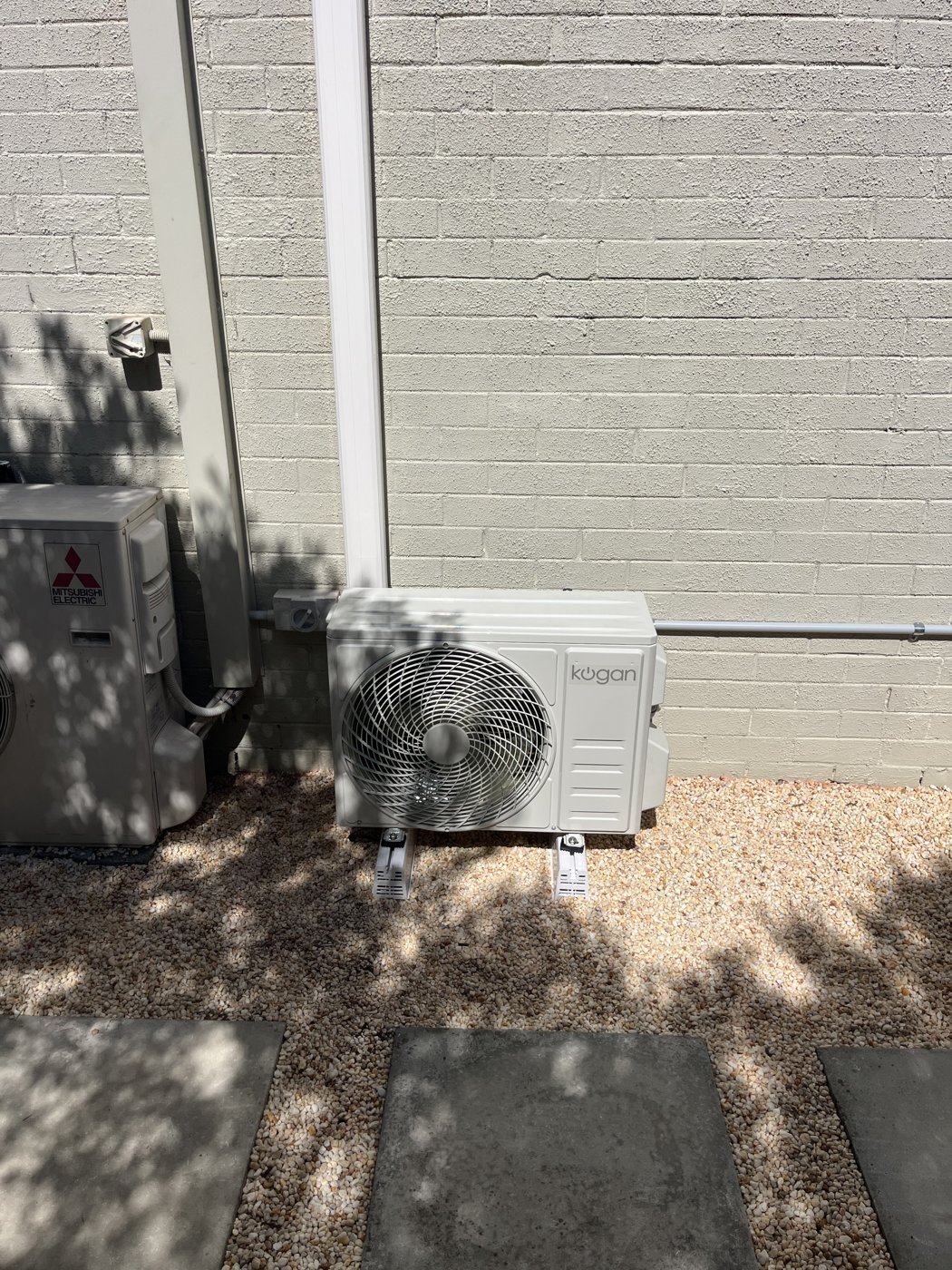 Kogan split system outdoor condenser unit installed on a rendered brick wall